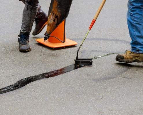 Person Using Tools To Fill Cracks In Asphalt Parking Lot